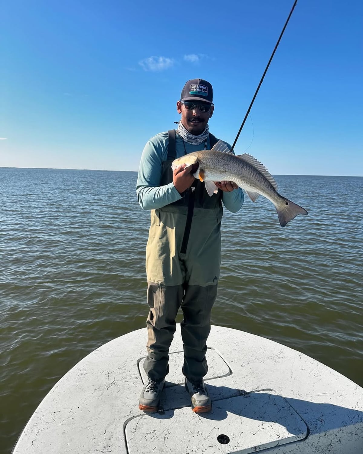 Captain Cody Simmons on the bay holding a redfish under a clear Texas sky