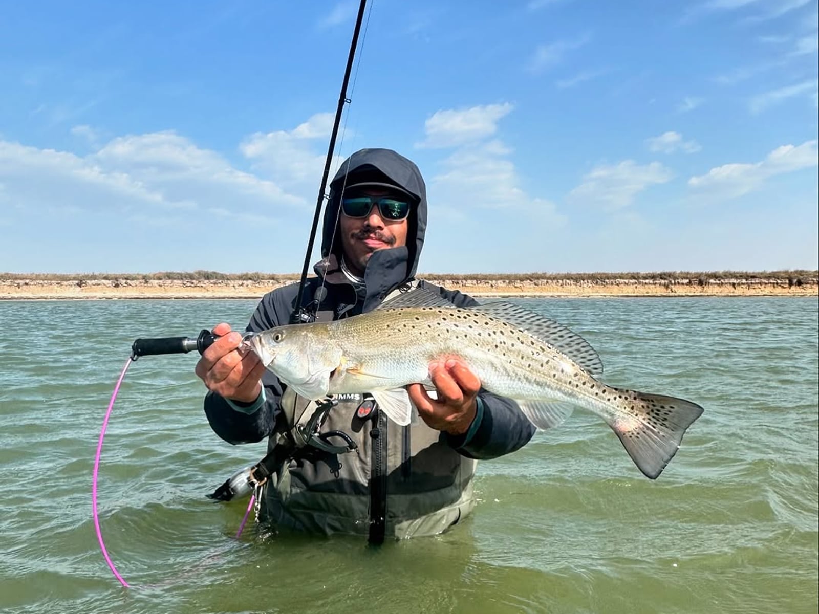 Angler wade fishing the Coastal Bend flats, holding a speckled trout against a blue sky