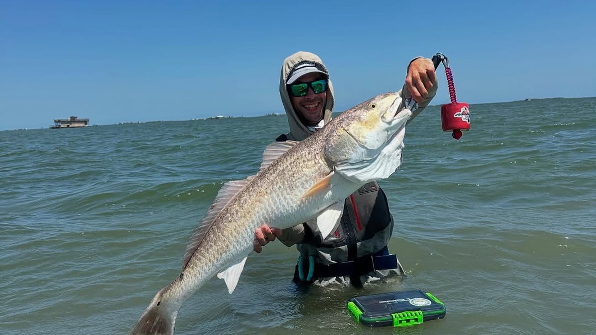 An angler wade fishing the open Texas bay holds up a bull redfish